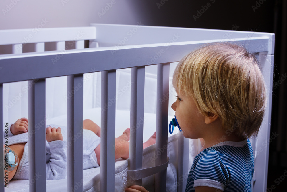 Toddler boy brother look in the crib of newborn sister Toddler boy brother look in the crib of newborn sister