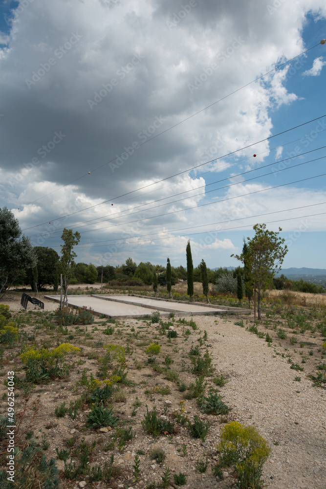 Des terrains de jeux de boules pétanque sont vus au milieu de la garrigues dans la nature sauvage entouré de cyprès et de végétation méditerranéenne.
