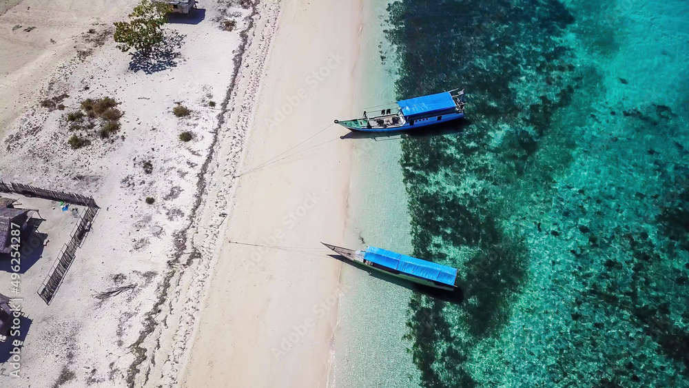Drone shot of two boats anchored to pink beach on an island near Maumere, Indonesia. There is a fisherman's cottage on the beach, separated by the fence. turquoise coloured water displaying coral reef Drone shot of two boats anchored to pink beach on an island near Maumere, Indonesia. There is a fisherman's cottage on the beach, separated by the fence. turquoise coloured water displaying coral reef