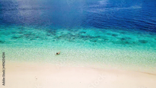 A drone shot of a girl playing on the beach on a small island near Maumere, Indonesia. Happy and careless moments. The coast changes colors from white to turquoise and navy blue. There are few islands