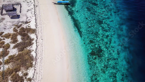 A drone shot of a boat anchored to pink beach on an island near Maumere, Indonesia. There is a fisherman's cottage on the beach, separated by the fence. turquoise coloured water displaying coral reef photo