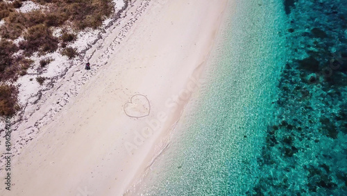 A drone shot of a heart drawn on the sand a small island near Maumere, Indonesia. Happy and careless moments. Waves gently washing the shore. Romance and love