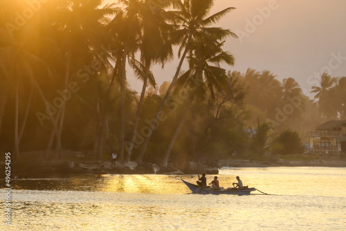 A sunset in Maumere, Flores, Indonesia. The sun sets behind the slope of the island. Serenity and calmness. There are few fishermen fishing from their boats in the bay. Palm trees growing on the shore photo