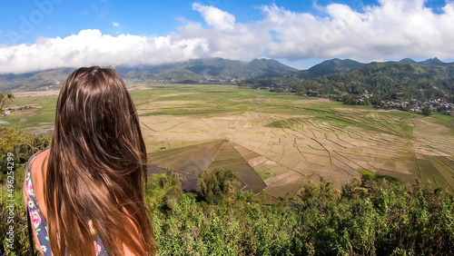 A woman in a jumpsuit admiring the colorful rice paddies forming a giant spider web in Ruteng, on island of Flores, Indonesia. There are mountains around the paddies. Lingko Spider Web Rice Fields photo