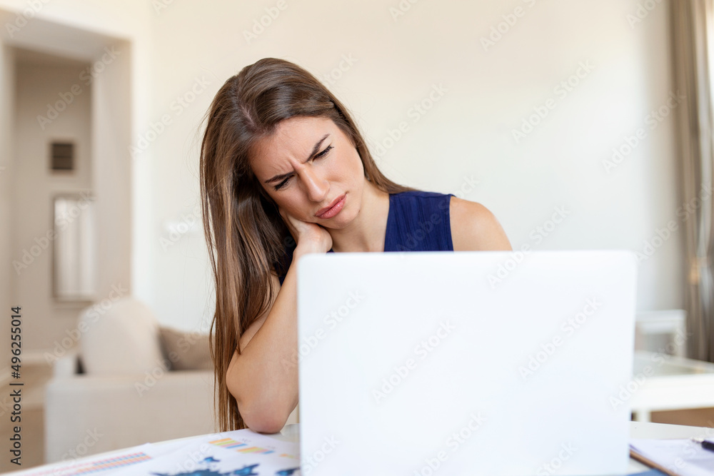 Feeling exhausted. Frustrated young woman looking exhausted and massaging her neck while sitting at her working place Feeling exhausted. Frustrated young woman looking exhausted and massaging her neck while sitting at her working place