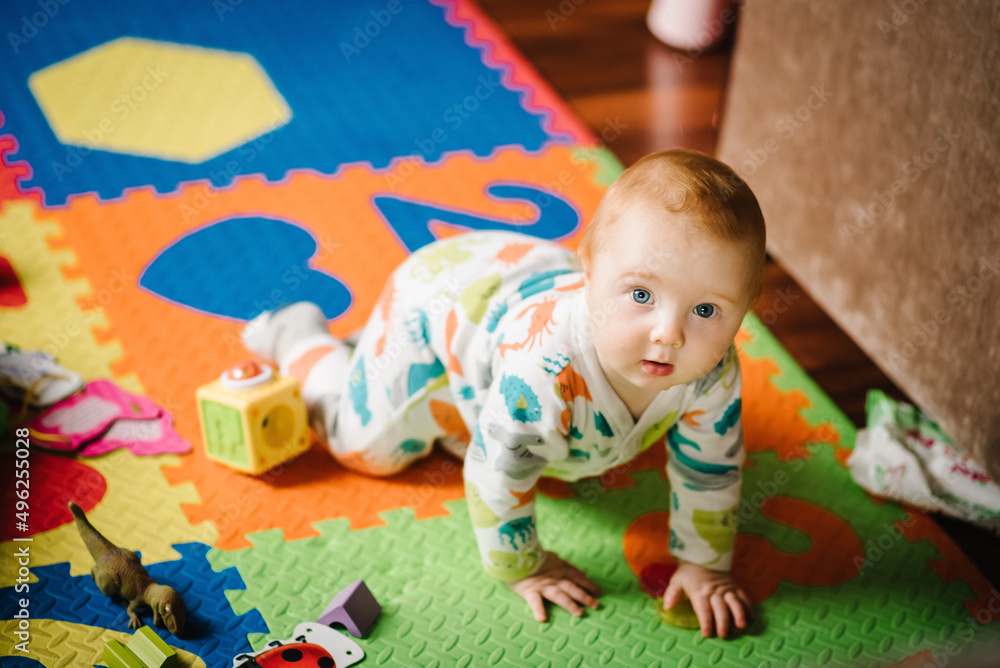The infant is playing with toys on the rug. Funny baby boy crawling on the floor in nursery room at home. Baby health care and family concept. The infant is playing with toys on the rug. Funny baby boy crawling on the floor in nursery room at home. Baby health care and family concept.