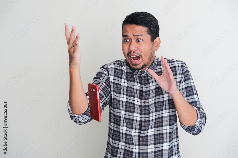 Adult Asian man showing shocked face expression when mobile phone fall from his hand Adult Asian man showing shocked face expression when mobile phone fall from his hand