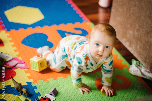 The infant is playing with toys on the rug. Funny baby boy crawling on the floor in nursery room at home. Baby health care and family concept.