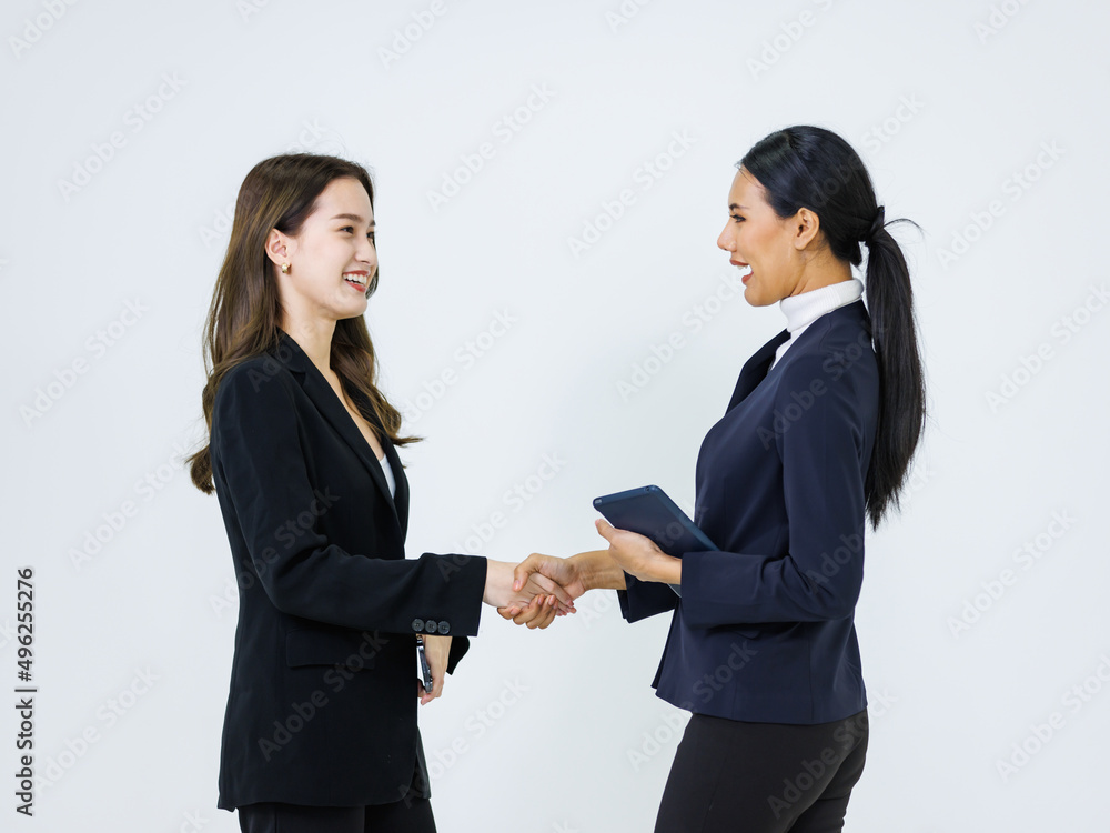 Studio shot of two Asian professional successful businesswoman in formal business suit standing shaking hands greeting say hi hello together on white background.