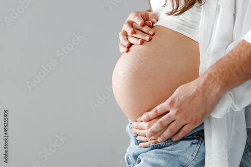 Happy pregnant woman in a studio with husband holding her stomach from behind and wearing bright shirt