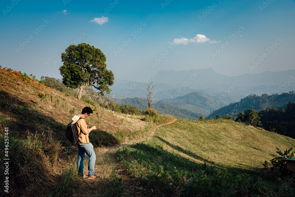 A man in a yellow shirt with a white hat is looking at a compass on golden dry grasslands at Hadubi, Chiang Mai, Thailand. A man in a yellow shirt with a white hat is looking at a compass on golden dry grasslands at Hadubi, Chiang Mai, Thailand.