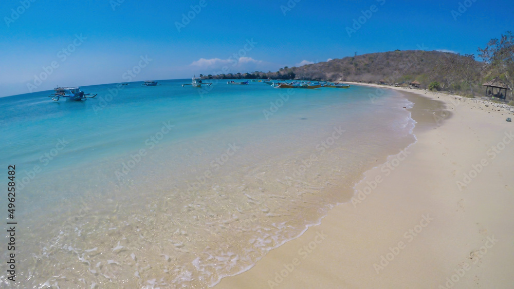 An areal, drone shot with a view on an idyllic Pink Beach on Lombok, Indonesia. Many boats drifting on a calm surface of the sea. Unspoiled, hidden gem. Perfect place for peaceful, relaxed holidays