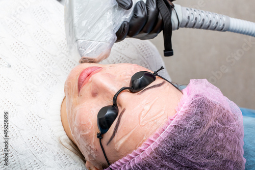 Cosmetic lifting procedure with a laser device. Anti-aging facelift, collagen and elastin production for facial rejuvenation. The girl is carried over her face with a laser device.