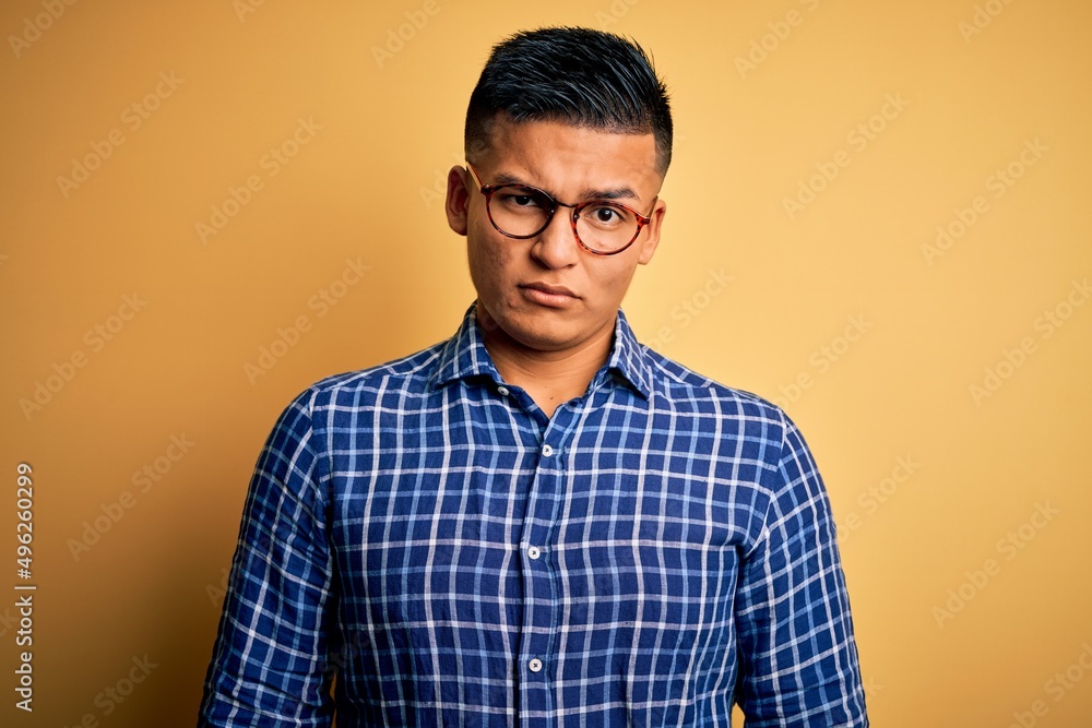 Young handsome latin man wearing casual shirt and glasses over yellow background skeptic and nervous, frowning upset because of problem. Negative person. Young handsome latin man wearing casual shirt and glasses over yellow background skeptic and nervous, frowning upset because of problem. Negative person.