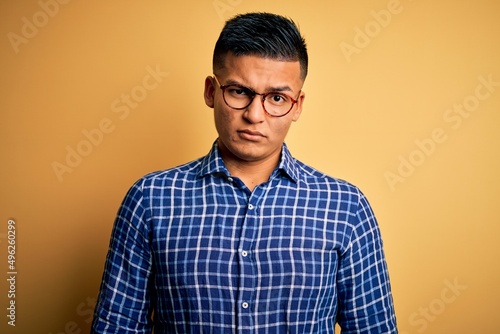 Young handsome latin man wearing casual shirt and glasses over yellow background skeptic and nervous, frowning upset because of problem. Negative person. © Fernando