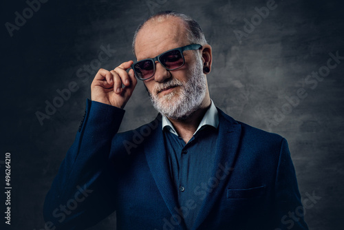 Bearded old man with sunglasses posing against dark background
