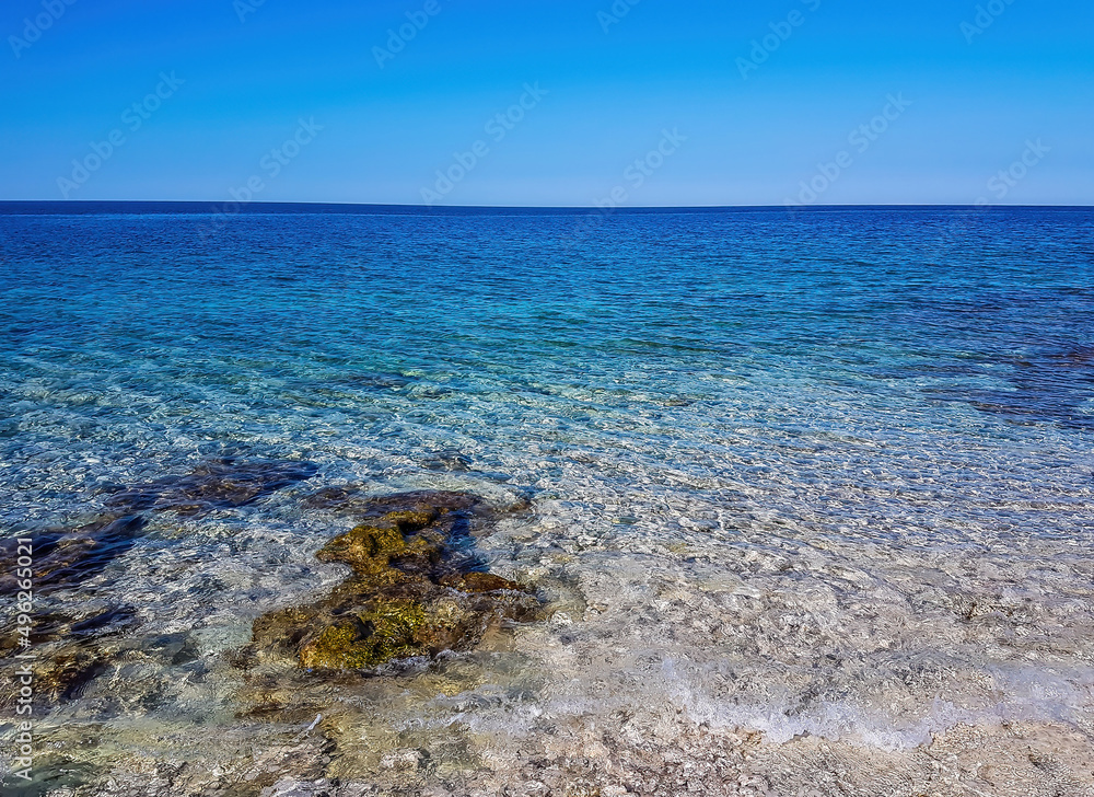 Calm, shallow sea water. There are barely any waves on the surface. The water is very clear, one can see the stony bottom. Few bigger stones protrude from water.