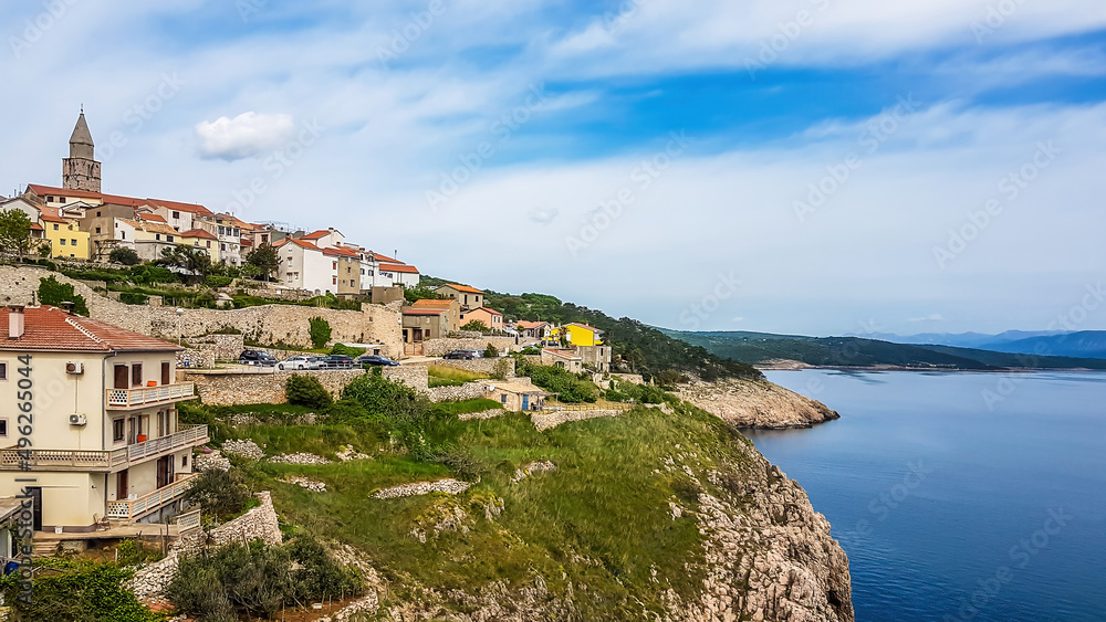 A remote view on a city located on a hill. In the middle of the city there is a tall bell tower. The houses are painted beige with orange rooftops. City located by the sea. Mediterranean culture.