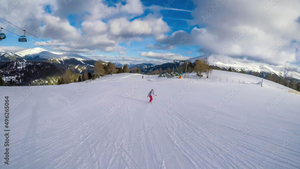 A snowboarder going down the slope in Turrach, Austria. Perfectly groomed slopes. High mountains surrounding the woman wearing pink trousers and colorful jacket. Girl wears helm for the protection. A snowboarder going down the slope in Turrach, Austria. Perfectly groomed slopes. High mountains surrounding the woman wearing pink trousers and colorful jacket. Girl wears helm for the protection.