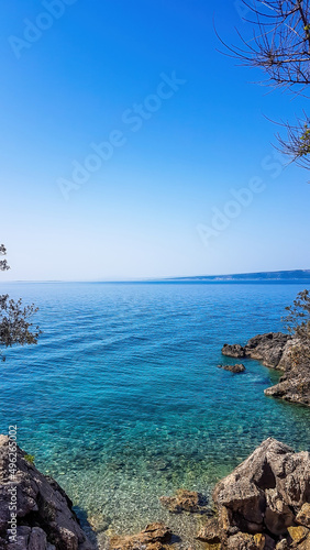 A view on a shallow water in a bay. Sea water is calm and shining with many shades of blue. On the side there are rocks striking out of the sea water, overgrown with trees. Clear and sunny weather. photo