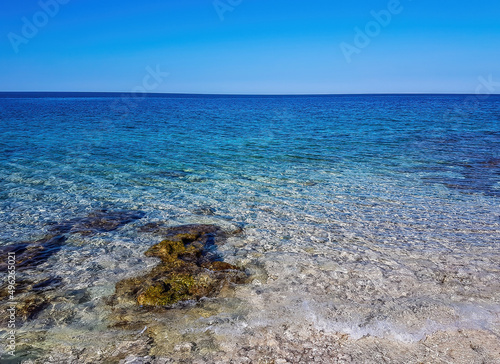 Calm, shallow sea water. There are barely any waves on the surface. The water is very clear, one can see the stony bottom. Few bigger stones protrude from water. photo