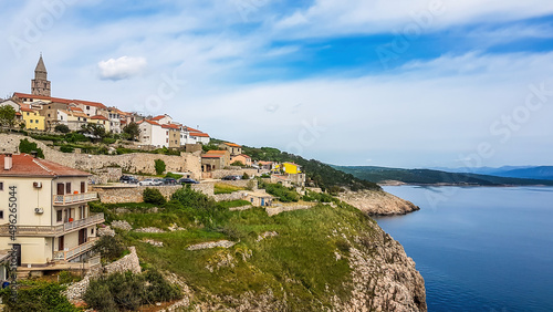 A remote view on a city located on a hill. In the middle of the city there is a tall bell tower. The houses are painted beige with orange rooftops. City located by the sea. Mediterranean culture.