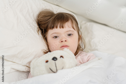 A girl with down syndrome lying on the bed under the covers and getting ready for bed. Usually childhood in a family