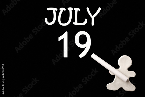 A small white plasticine man writing the date 19July on a black board. Business concept. Education concept. photo