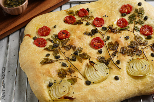 Floral painting focaccia, italian garden flatbread art with barley, tomatoes, onions, sesame seeds and capers on light grey background photo