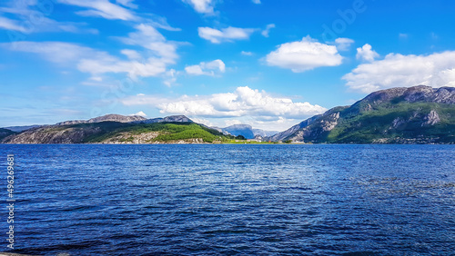 A wast fjord near Rogaland, Norway. Water of the fjord is slightly wavy. Bright sunbeams reflect in the water's surface. In the back tall mountains are shrouded in fog. photo