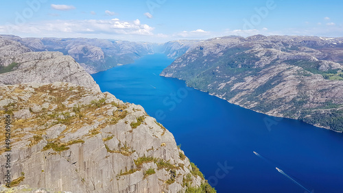 A stunning view on Lysefjorden from Preikestolen. Surface of the water located 600m below. A ship moving through it. Steep cliffs are joining the water on both sides. A bit of mist in the back.