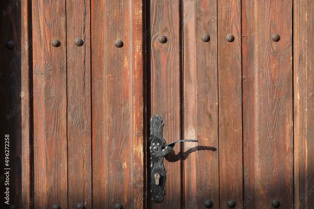 Wooden brown front door with old rusty black handle and lock closeup in sunlight as background Wooden brown front door with old rusty black handle and lock closeup in sunlight as background