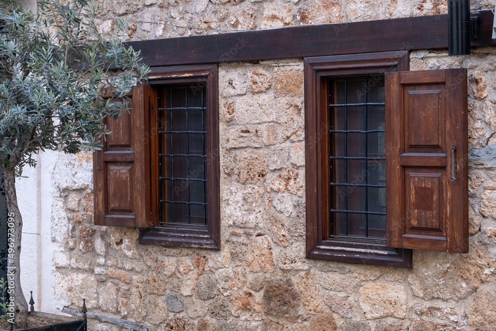 Stone ancient building with wooden frames next to a tree in a flower bed in the old town Stone ancient building with wooden frames next to a tree in a flower bed in the old town
