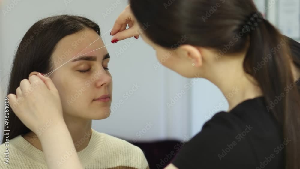 professional correction eyebrows shape, removing unwanted hair using thread, threading brows beauty salon. beautician stylist makes eyebrows removing with string. caucasian female close-up face brows professional correction eyebrows shape, removing unwanted hair using thread, threading brows beauty salon. beautician stylist makes eyebrows removing with string. caucasian female close-up face brows