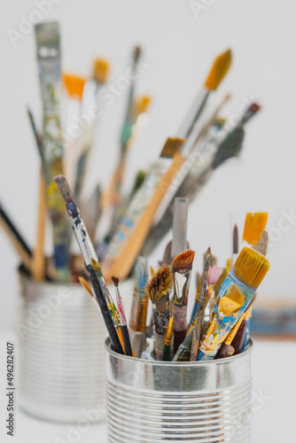 Collection of bristles or painting brushes. Artist bristle or brush covered in paint safely stored in aluminium can on a white background.