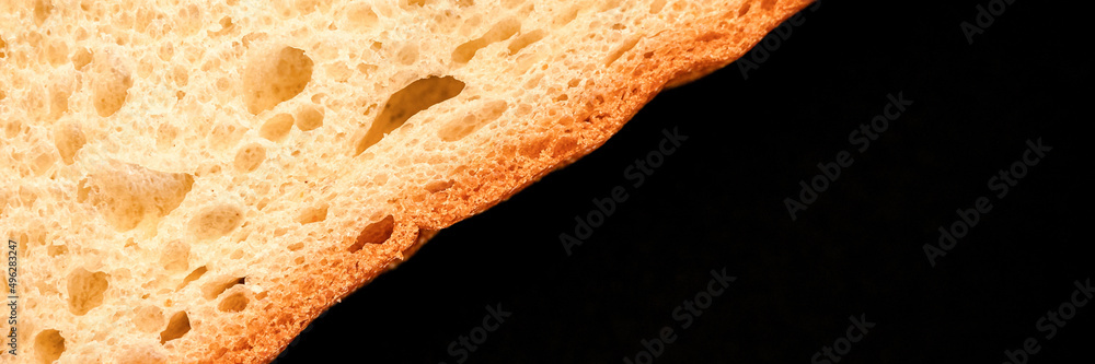 slice of white bread close up isolated on a black background. rough textured surface chopped piece loaf of natural organic food with holes. top view. abstract concept of the planet and space. banner