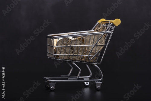 Side view of bitcoin and shopping cart on black background. Buying or selling the cryptocurrency concept. Virtual money, cryptocurrency. E-commerce concept.
