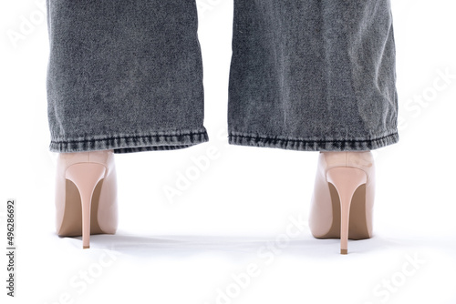 Women's legs in elegant patent leather high-heeled beige shoes. Gray wide leg jeans. View from