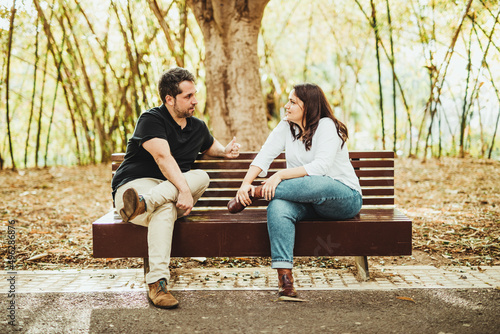 Friends sitting on a bench in a park with trees talking and arguing