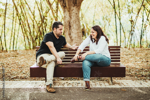 Friends sitting on a bench in a park with trees talking and smiling
