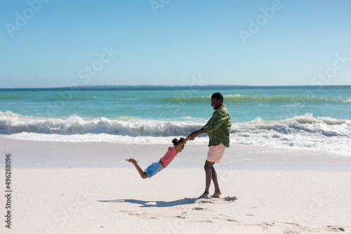 Happy african american man spinning daughter at beach while enjoying summer holiday together