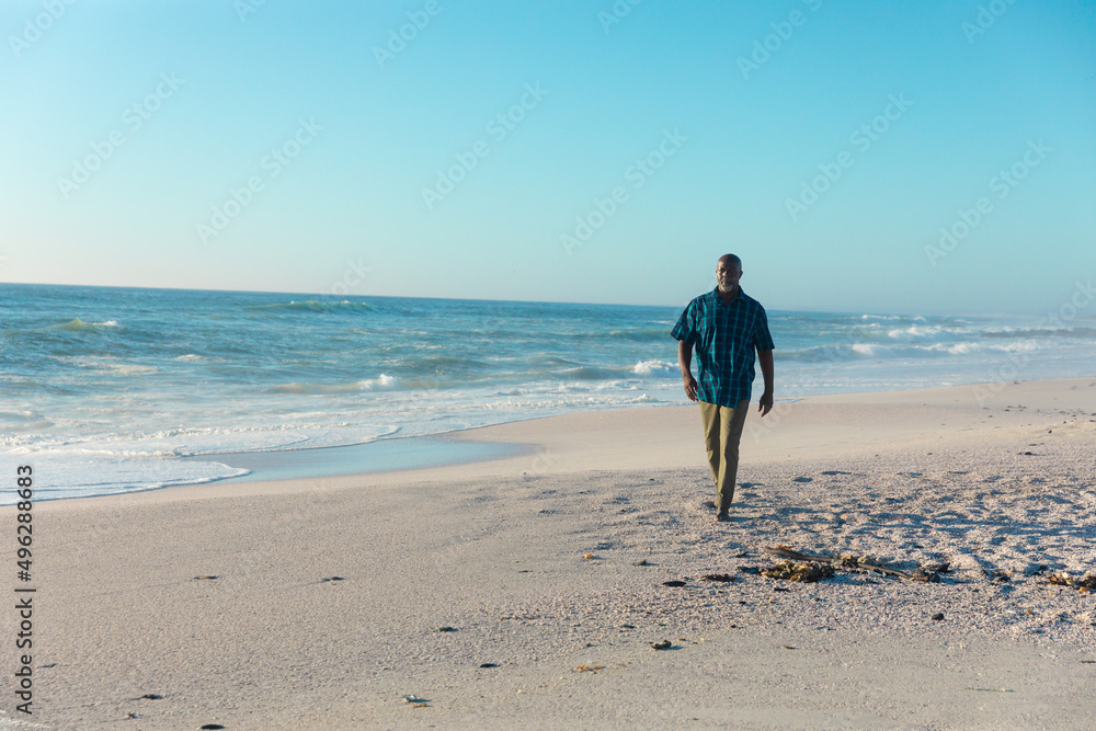 Full length of retired african american senior man walking on shore at beach with copy space Full length of retired african american senior man walking on shore at beach with copy space