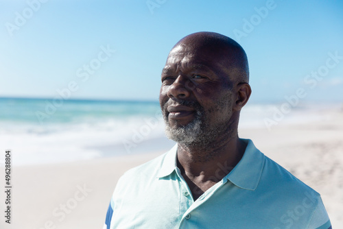 Confident african american retired senior bald man looking away at beach on sunny day