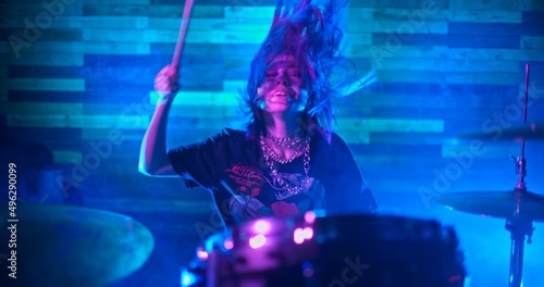 Drummer girl energetically playing the drums in blue, red and green lights. photo