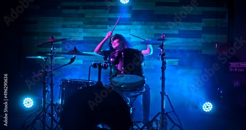 Drummer girl energetically playing the drums in blue lights on stage during show