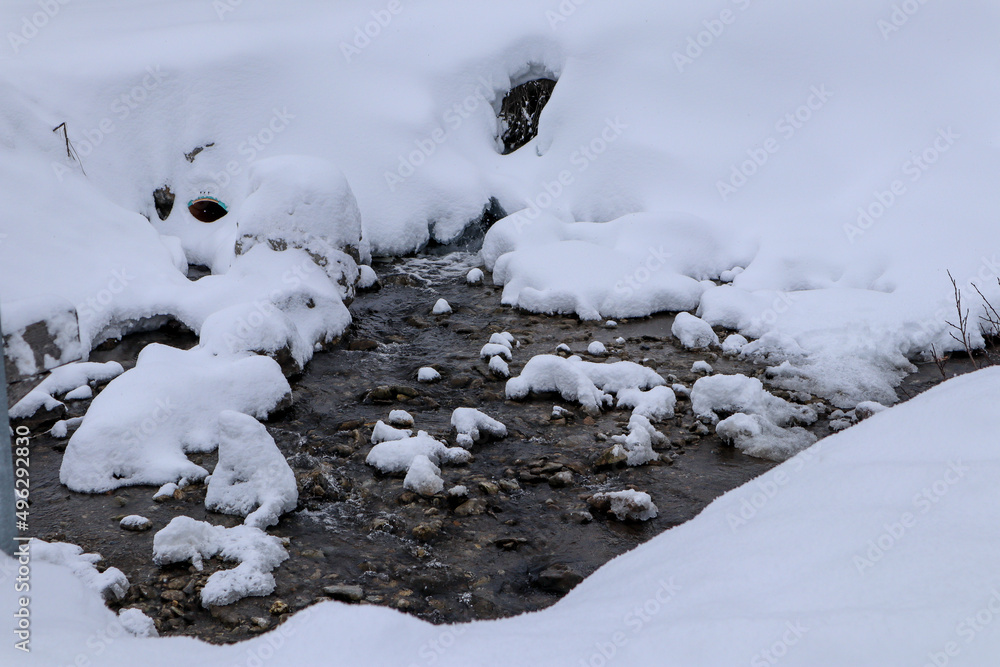 A small River flowing through the snow in Churwalden, Switzerland A small River flowing through the snow in Churwalden, Switzerland