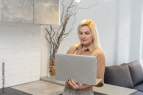 Nice beautiful blonde lady works at the notebook sit down on the sofa at home - check on oline shops for cyber monday sales - technology woman concept for alternative office freelance photo