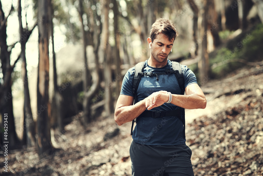 Obraz premium Checking his time. Cropped shot of a handsome young man checking his watch while out hiking in the mountains.