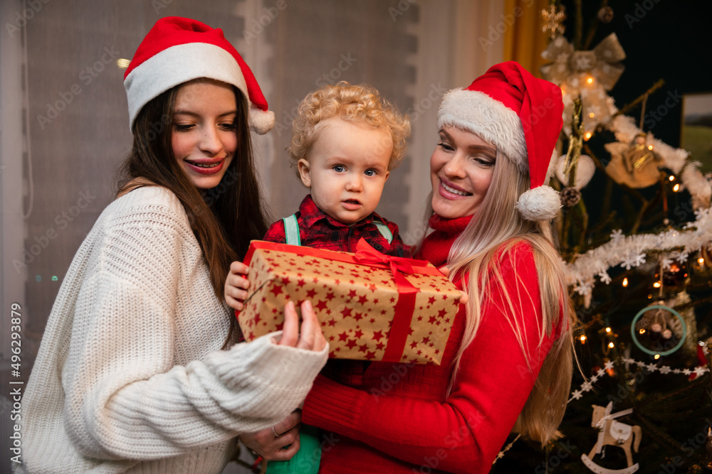 A mom and big sister give a gift to a two-year-old child at Christmas. A mom and big sister give a gift to a two-year-old child at Christmas.