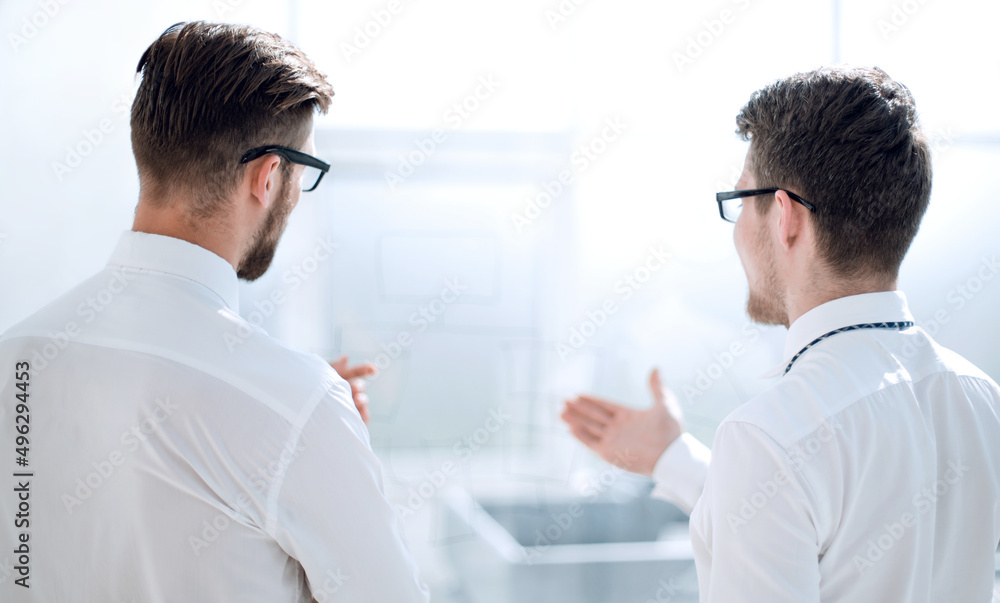 rear view.business colleagues talk standing in a bright office rear view.business colleagues talk standing in a bright office